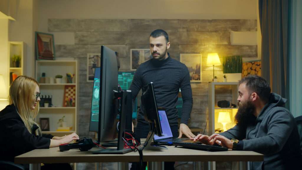 Three professionals work at desktop computers in an office, representing the collaboration involved in software development.